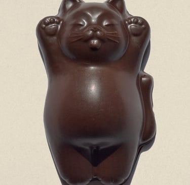 A brown chocolate maneki-neko lucky cat figurine with raised paws on a beige background.