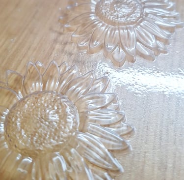 Clear plastic sunflower molds with textured petals and center seeds on a wooden surface.