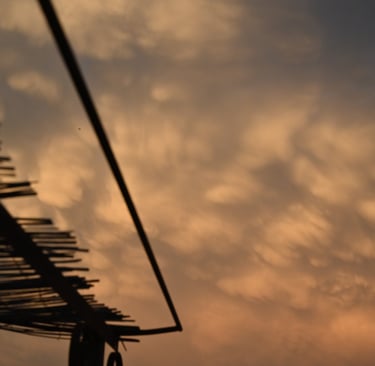 Golden mammatus clouds at sunset viewed from beneath a rustic bamboo roof structure.