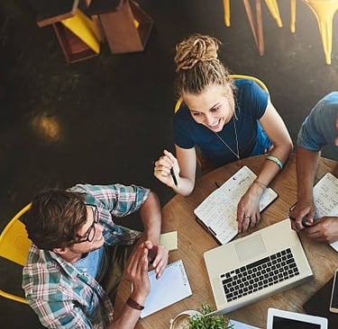 Overhead shot of three smiling university students studying together at a coffee shop table, with a 