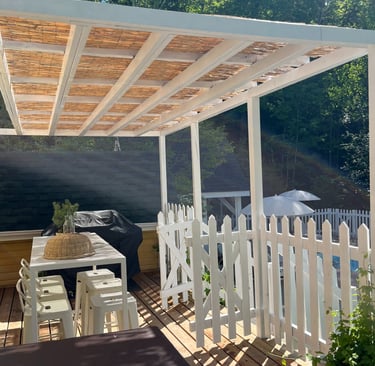 a patio with a pergola,  table and chairs and a grill
