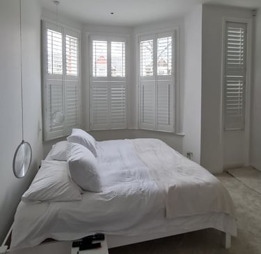 Beautifully restored plantation wood shutters on a bay window in a bright Twickenham bedroom