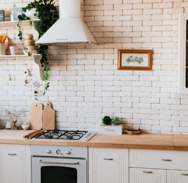Cozinha clara com armários brancos, bancada de madeira e decoração com plantas e utensílios