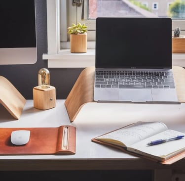 Home office compacto com suporte para notebook, caderno e decoração com plantas.