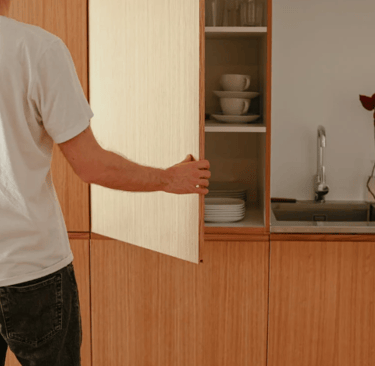 Homem abrindo armário de cozinha planejada em ambiente minimalista com madeira clara.