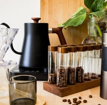 Itens de preparo de café em bancada de madeira com plantas decorativas ao fundo.
