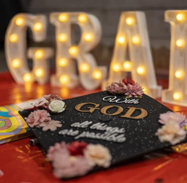 Graduation cap laying on table with the word GRAD lit up behind it.