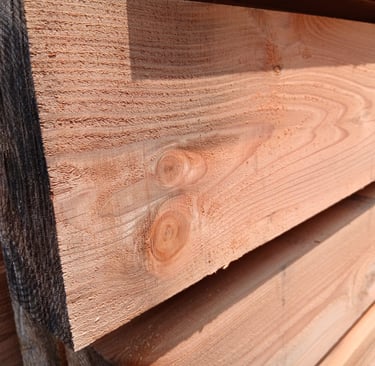 Stacked rough-cut cedar lumber showing natural wood grain and knots for construction projects.