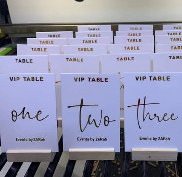 Assorted white Acrylic Table Numbers with black and gold script, labeled from 'one' to 'four' 