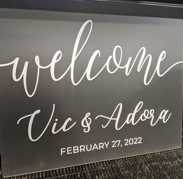 Gray acrylic welcome sign with 'Vic & Adora, February 27, 2022' in white script, ready for a wedding