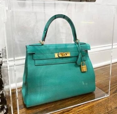 Teal designer handbag showcased in clear acrylic box.