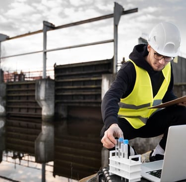 a man in a hardhat with a clipboard taking a sample of water by the river