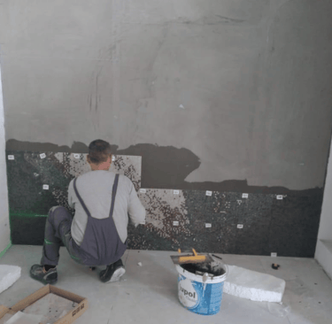 Fliesenleger befestigt nummerierte Glasmosaik-Platten auf vorbereiteter Wandfläche.