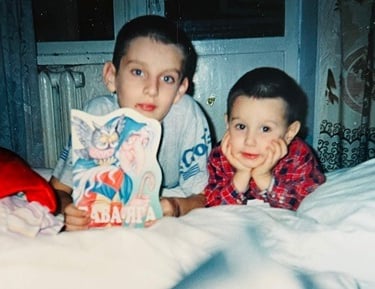 Two young brothers at bedtime: the elder holds a picture book, and the younger smiles at the camera.