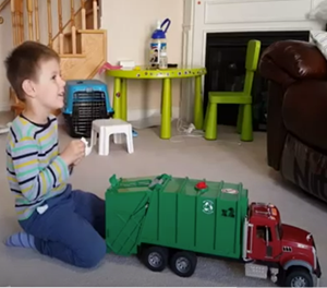 A young boy happily playing with a green toy garbage truck in a cozy living room.