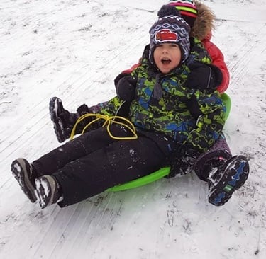 Two children sledding down a snowy hill, bundled up in winter gear, laughing joyfully.