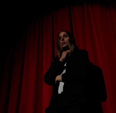 Aodh, played by Finn Rooney, standing in front of a red velvet curtain in a theatre