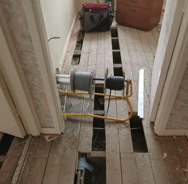 Electrical cable reels on a stand over exposed wooden floorboards during a home renovation.