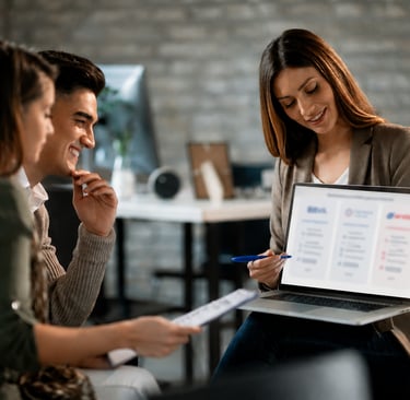 A financial advisor showing a digital business presentation on a laptop to a young couple in a modern office.