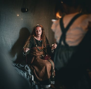 A woman in a Viking age dress sitting on a bench using a spindle