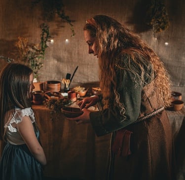 a woman in a dress holding a bowl is talking to a little girl in front of a table of herbal remedies