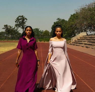 Two women in elegant evening gowns walking on a red running track at an outdoor stadium.
