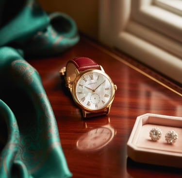 Luxury gold watch with leather strap on a vanity next to diamond earrings and silk scarf.