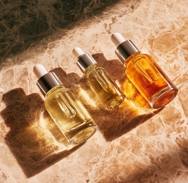 Three glass dropper bottles of facial oil and serum on a luxury marble surface with sunlight shadows.