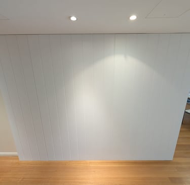 Modern white vertical shiplap accent wall with recessed spotlighting and oak hardwood flooring.