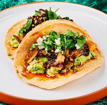 two vegan tacos on a plate with a green table cloth