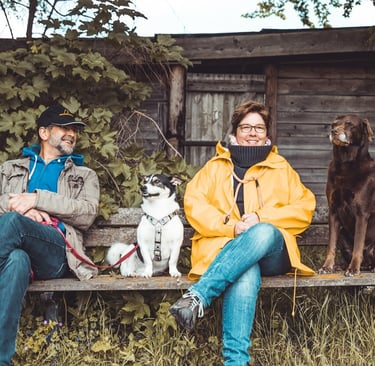 Marion und Martin Lindhof auf einer Bank im Wald mit Labradorhündin Amy und Pensionshund Trapper.