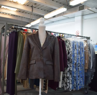 Maniquí con chaqueta corta de polipiel marrón. Fondo con perchas con ropa