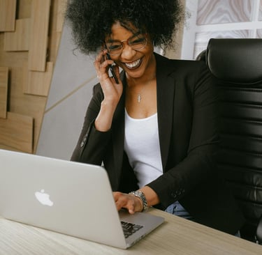 a woman sitting at a desk with a laptop and a cell phone