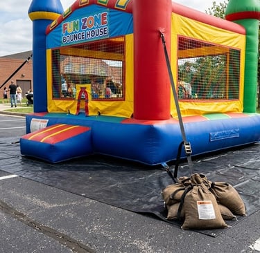 Bounce house anchored on reinforced tarp on pavement with sandbags