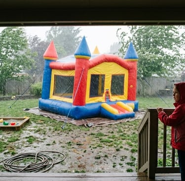 bounce house in heavy winds and rain in backyard with kids looking at it from porch