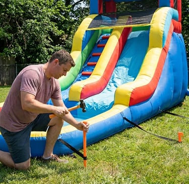 parent anchoring an inflatable water slide with a splash pool in a backyard