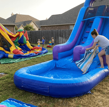parent drying a water slide with a towel while a bounce house deflates nearby