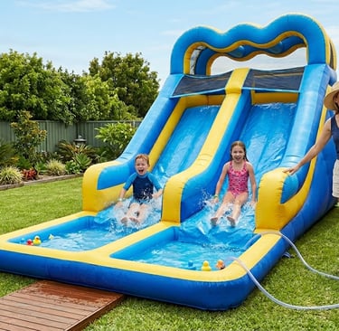 parents supervising two kids on an inflatable dual‑lane water slide in the backyard