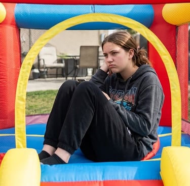 teenage girl playing in toddler size bounce house, looking bored