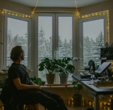 Man sitting in a softly lit room, looking out snowy windows in quiet reflection.
