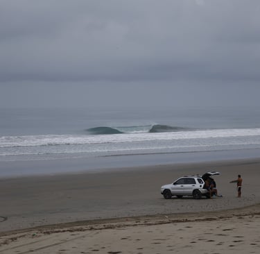 A perfect unridden wave with surfers watching from the beach