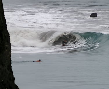 A bodyboarder riding a wave and another surfer watching from the water