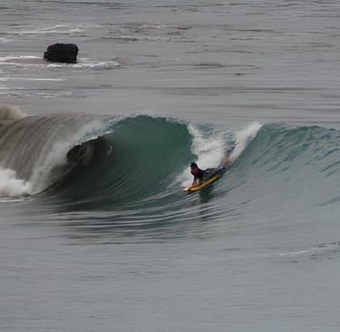 A bodyboarder riding a wave and another surfer watching from the water