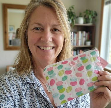 Smiling woman holding a handmade quilted makeup bag with a colorful macaron print pattern.