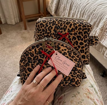 Two leopard print quilted makeup bags with red ribbons and brand tags resting on a person's lap.