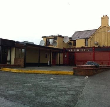 Exterior view of Aherne's pub in Tallaght with a red frontage and outdoor seating area.