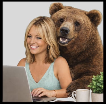Smiling woman working on a laptop with a large brown grizzly bear looking over her shoulder.