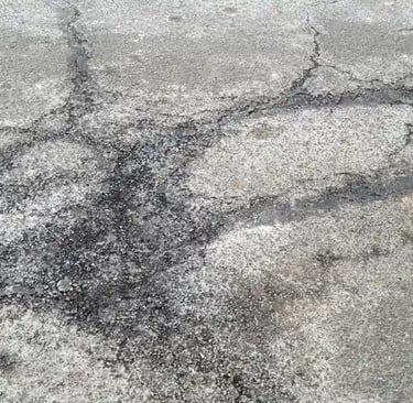Worn asphalt surface showing winter damage from snow plows, salt, and freeze thaw cycles affecting 