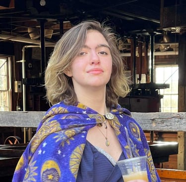 teenager with brown and blond shoulder-length hair wearing a celestial cape and a proud expression