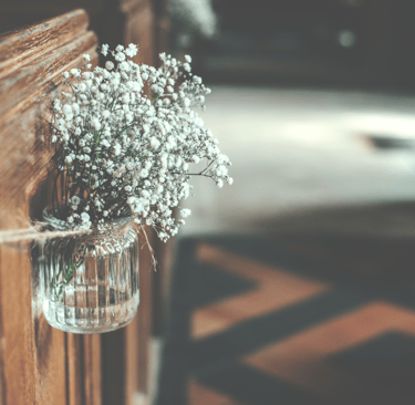 un vase avec des fleurs de gypsophile sur un banc d'église